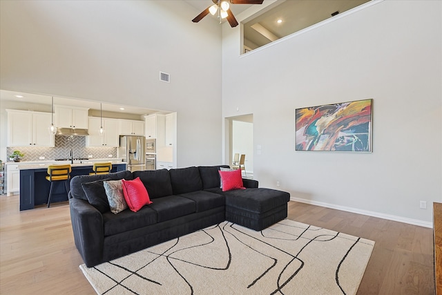 living room with beam ceiling, high vaulted ceiling, light hardwood / wood-style flooring, and ceiling fan