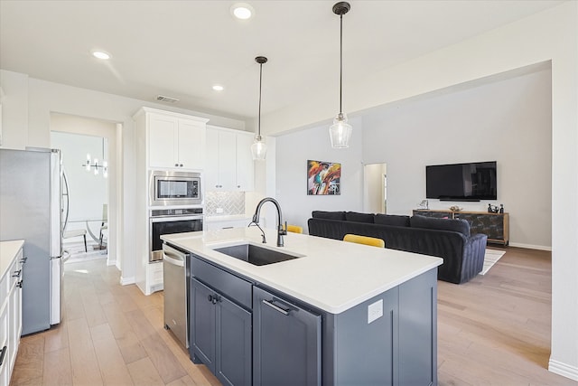 kitchen with white cabinetry, sink, stainless steel appliances, light hardwood / wood-style flooring, and a center island with sink