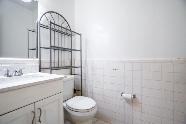 bathroom featuring toilet, wainscoting, tile walls, and vanity