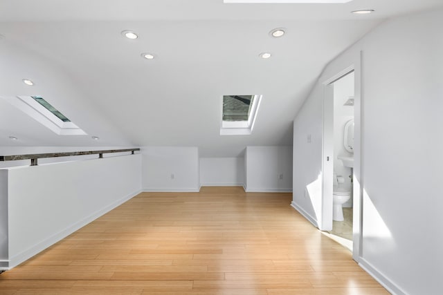 additional living space featuring light hardwood / wood-style floors and vaulted ceiling with skylight