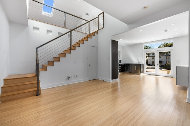 unfurnished living room featuring a high ceiling, sink, french doors, and light hardwood / wood-style flooring