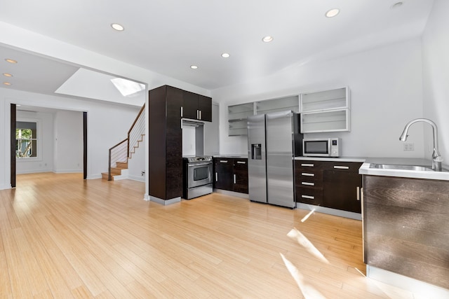 kitchen featuring stainless steel appliances, light wood-type flooring, dark brown cabinetry, sink, and a skylight