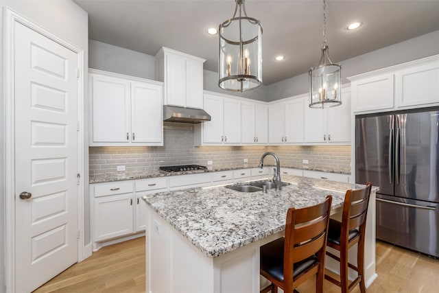 kitchen featuring stainless steel refrigerator, sink, decorative light fixtures, a kitchen island with sink, and light hardwood / wood-style flooring