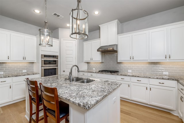 kitchen featuring white cabinetry, a center island with sink, sink, and pendant lighting