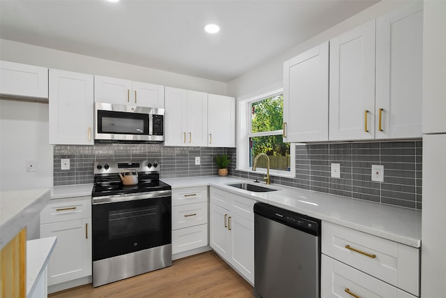 kitchen featuring stainless steel appliances, sink, white cabinets, light wood-type flooring, and decorative backsplash