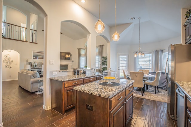 kitchen with appliances with stainless steel finishes, dark wood-type flooring, pendant lighting, high vaulted ceiling, and a center island