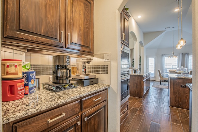 kitchen with dark wood-type flooring, tasteful backsplash, decorative light fixtures, light stone counters, and a chandelier