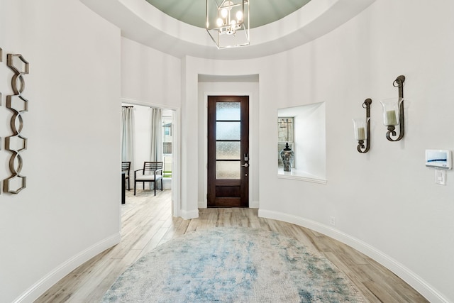 entryway with a high ceiling, a tray ceiling, a notable chandelier, and light hardwood / wood-style floors