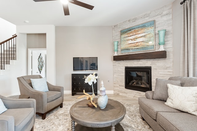 living room with a stone fireplace, wood-type flooring, and ceiling fan