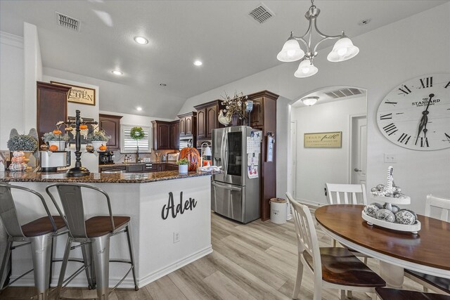 kitchen with stainless steel fridge, dark stone counters, hanging light fixtures, dark brown cabinetry, and light hardwood / wood-style floors