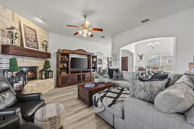 living room featuring crown molding, a stone fireplace, ceiling fan with notable chandelier, and light wood-type flooring