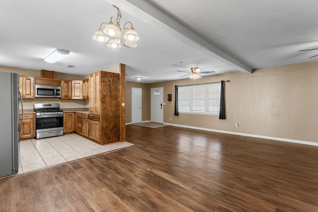 kitchen with stainless steel appliances, light hardwood / wood-style floors, ceiling fan with notable chandelier, beam ceiling, and a textured ceiling