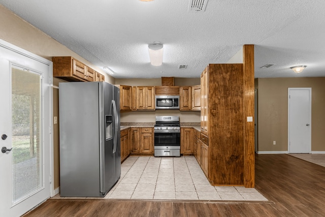 kitchen with a textured ceiling, light hardwood / wood-style flooring, and appliances with stainless steel finishes