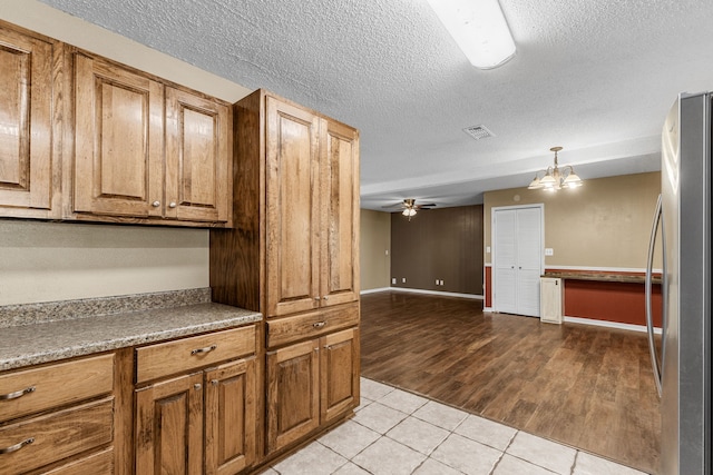 kitchen featuring ceiling fan with notable chandelier, light hardwood / wood-style floors, a textured ceiling, pendant lighting, and stainless steel fridge