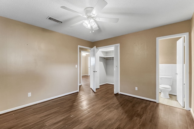 unfurnished bedroom with ceiling fan, connected bathroom, a closet, and dark hardwood / wood-style flooring