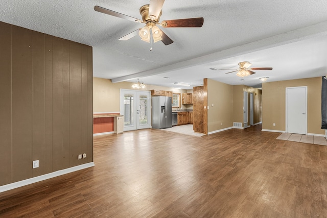 unfurnished living room with ceiling fan with notable chandelier, light hardwood / wood-style floors, a textured ceiling, wooden walls, and beam ceiling