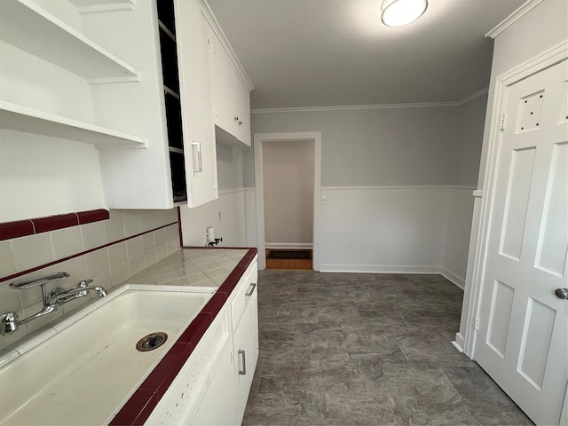 kitchen featuring tile countertops, backsplash, sink, ornamental molding, and white cabinetry