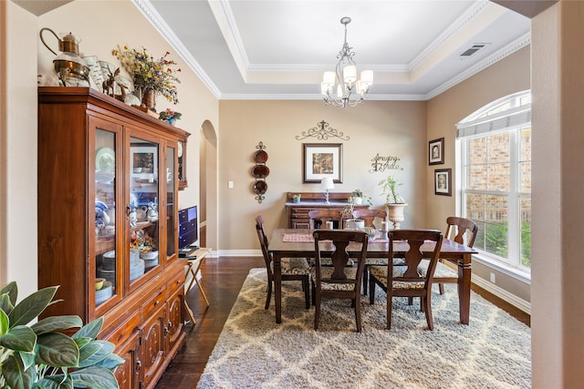 dining room with ornamental molding, a tray ceiling, dark wood-type flooring, and a notable chandelier