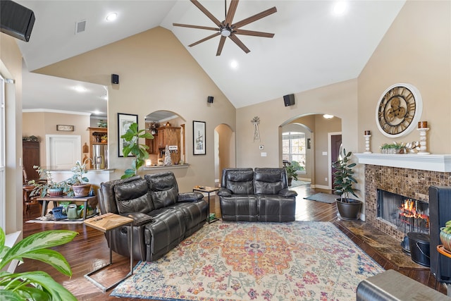 living room with high vaulted ceiling, crown molding, ceiling fan, dark hardwood / wood-style flooring, and a tiled fireplace