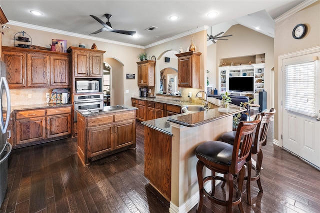 kitchen featuring kitchen peninsula, appliances with stainless steel finishes, a kitchen breakfast bar, dark wood-type flooring, and sink