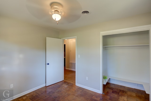 unfurnished bedroom featuring dark parquet flooring, ceiling fan, and a closet