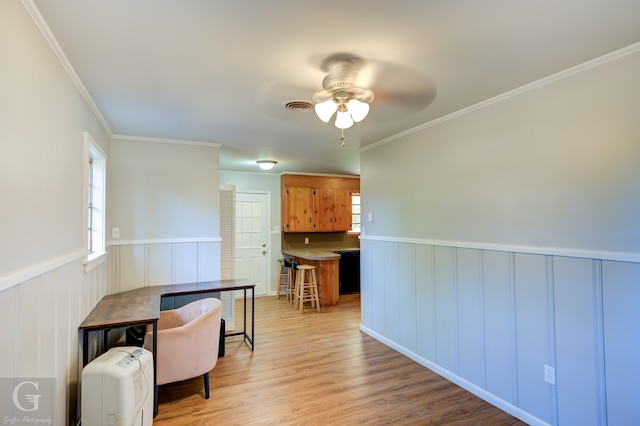 interior space with light hardwood / wood-style floors, ceiling fan, crown molding, and a breakfast bar area