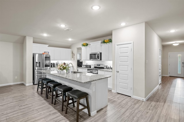 kitchen featuring stainless steel appliances, white cabinetry, a kitchen island with sink, and a breakfast bar area