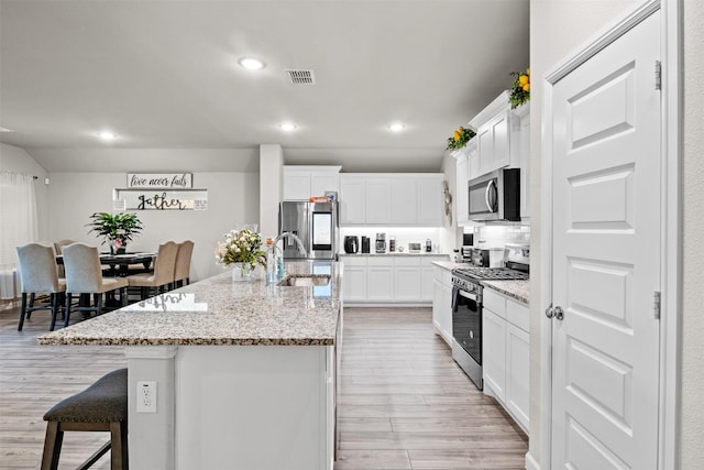 kitchen featuring light stone countertops, light hardwood / wood-style flooring, a center island with sink, white cabinets, and appliances with stainless steel finishes