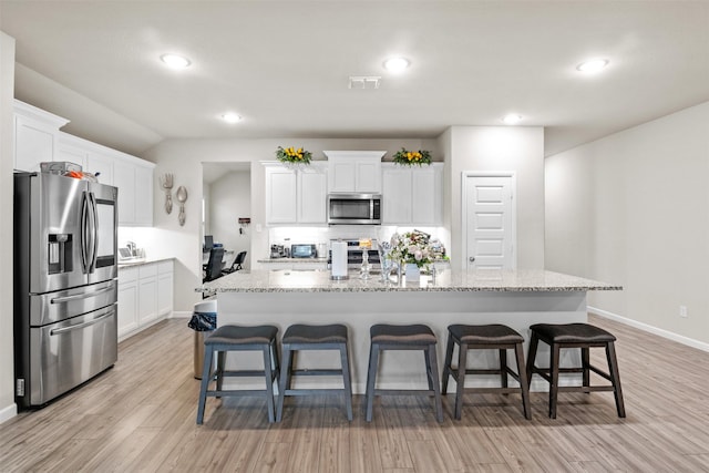 kitchen featuring a center island with sink, white cabinets, a kitchen bar, and appliances with stainless steel finishes