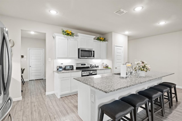 kitchen with stainless steel appliances, light hardwood / wood-style flooring, an island with sink, a breakfast bar area, and white cabinets