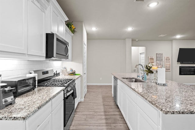 kitchen featuring white cabinetry, sink, stainless steel appliances, light hardwood / wood-style floors, and a center island with sink