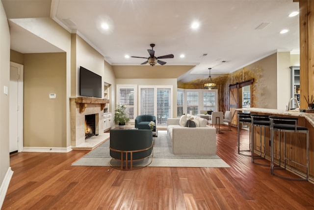 living room with hardwood / wood-style floors, ceiling fan, a fireplace, and ornamental molding