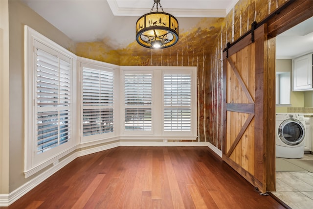 unfurnished dining area featuring a barn door, hardwood / wood-style flooring, crown molding, and washer / dryer