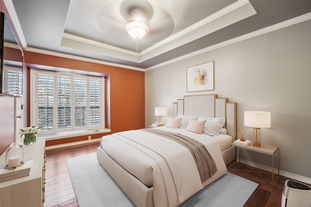 bedroom featuring dark hardwood / wood-style flooring, ornamental molding, ceiling fan, and a raised ceiling