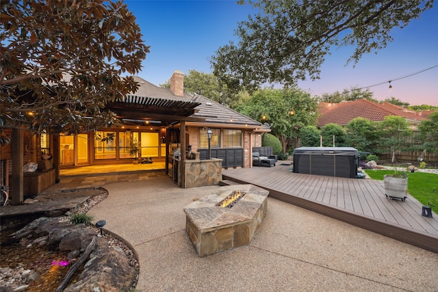 back house at dusk featuring a hot tub, a patio, an outdoor fire pit, and a wooden deck