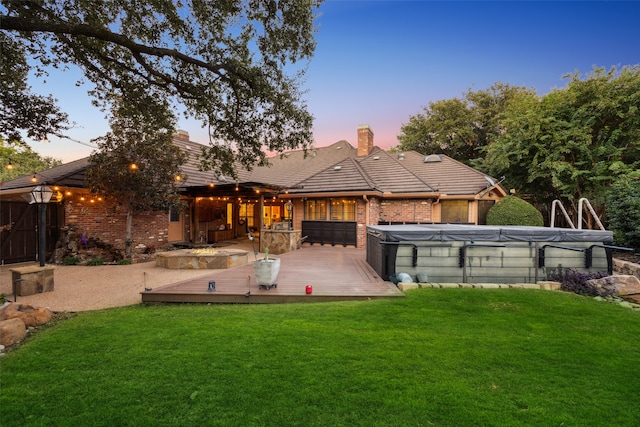 back house at dusk featuring a lawn and a pool side deck