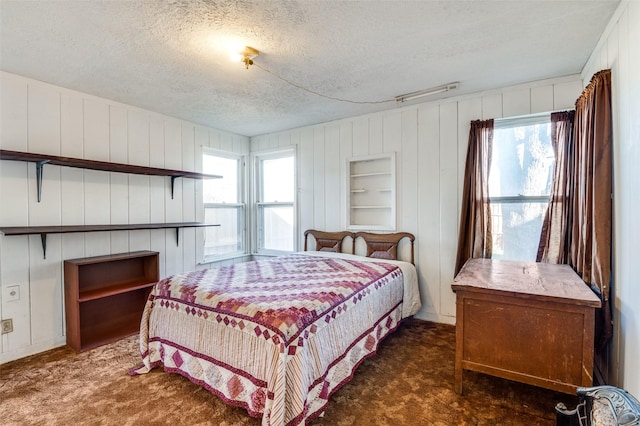 bedroom with multiple windows, wooden walls, dark carpet, and a textured ceiling