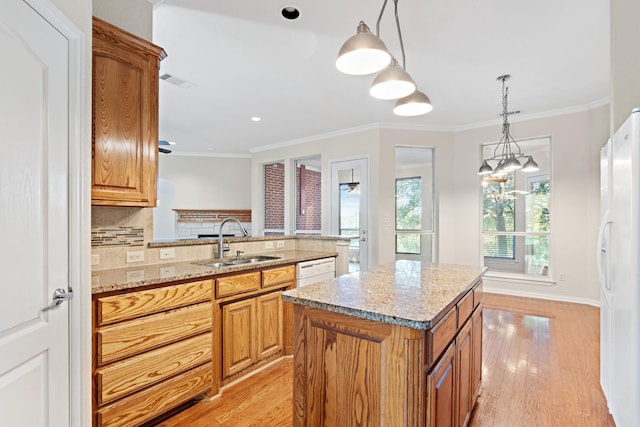 kitchen with light hardwood / wood-style floors, sink, a kitchen island, white appliances, and decorative light fixtures