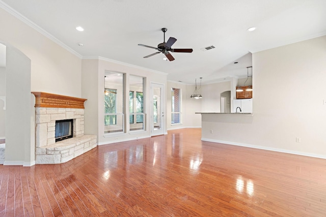 unfurnished living room featuring hardwood / wood-style floors, ceiling fan with notable chandelier, a fireplace, and crown molding