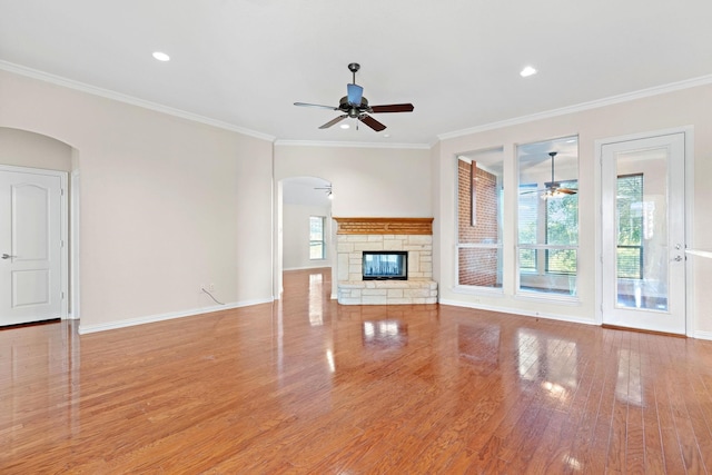 unfurnished living room featuring ceiling fan, a stone fireplace, light wood-type flooring, and crown molding