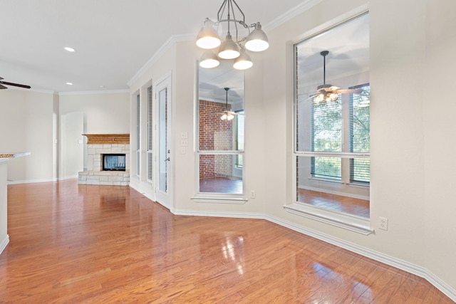 unfurnished dining area with a fireplace, ceiling fan with notable chandelier, ornamental molding, and light hardwood / wood-style flooring