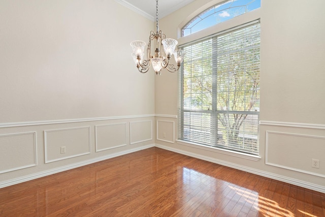 unfurnished room with wood-type flooring, a healthy amount of sunlight, a notable chandelier, and ornamental molding