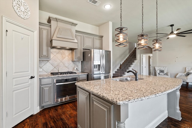 kitchen with sink, dark wood-type flooring, light stone counters, a center island with sink, and appliances with stainless steel finishes