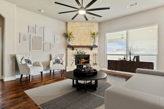 living room featuring ceiling fan, dark hardwood / wood-style floors, and a stone fireplace