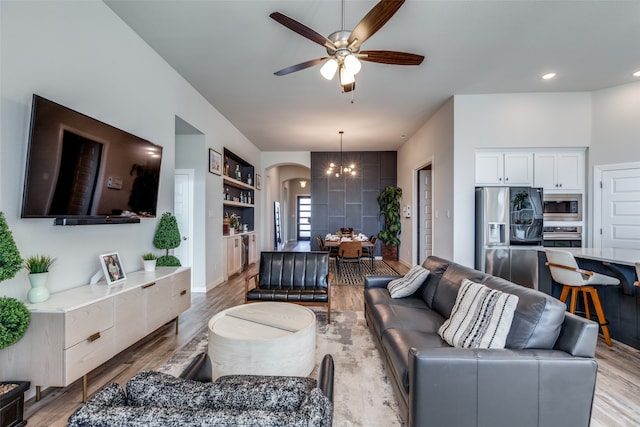 living room with light wood-type flooring, built in shelves, and ceiling fan with notable chandelier