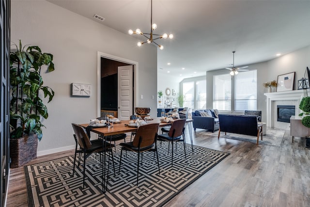 dining space with ceiling fan with notable chandelier and hardwood / wood-style floors