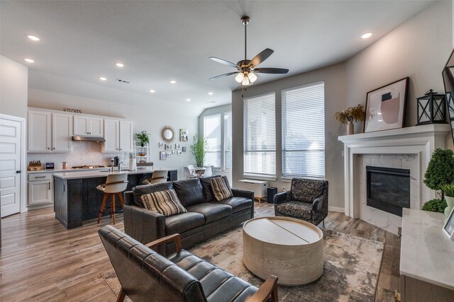 living room featuring a fireplace, light hardwood / wood-style flooring, lofted ceiling, and ceiling fan