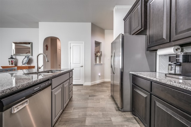 kitchen with sink, light hardwood / wood-style flooring, light stone countertops, dark brown cabinets, and stainless steel appliances