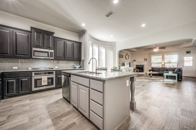 kitchen with a kitchen island with sink, sink, light hardwood / wood-style flooring, ceiling fan, and stainless steel appliances