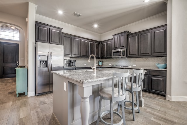 kitchen with light stone countertops, appliances with stainless steel finishes, a kitchen bar, sink, and an island with sink